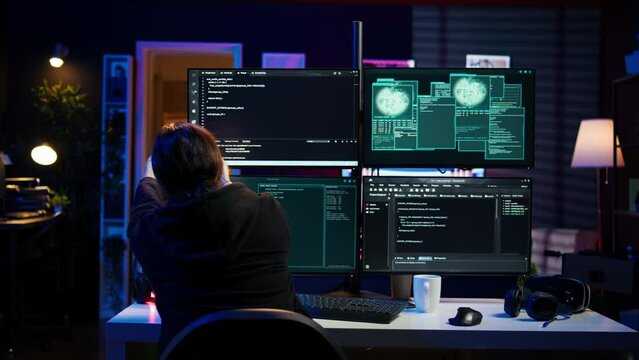 Dangerous hacker writing lines of code on PC from secret apartment, trying to get past security systems. Evil software developer building scripts that can hack devices, camera B