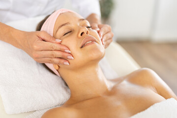Young woman enjoying professional facial massage to relieve muscle tension and improve skin...