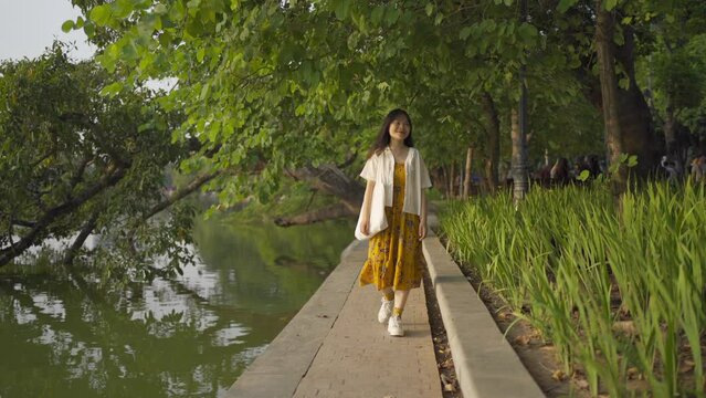 Portrait of happy Asian Vietnamese woman travel at Turtle tower in river of Hoan Kiem Lake in public park garden in Downtown Hanoi. Urban city, Vietnam. People lifestyle.