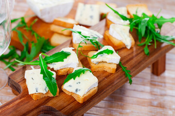 Freshly prepared sandwiches with blue cheese and green arugula on a wooden board