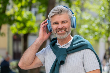 Happy mature Caucasian man in wireless headphones choosing, listening favorite energetic music in...