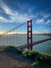 Northern tower of Golden Gate Bridge and partial cityscape of San Francisco, California, USA at sunrise against blue sky with clouds