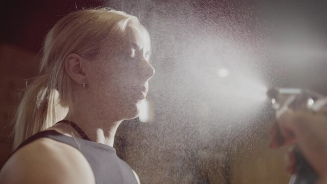 Female athlete sprayed in face with mist spray bottle to cool off from workout