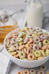 Tasty cereal rings in bowl, milk and honey on light table, closeup