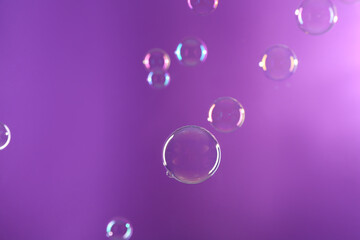 Beautiful transparent soap bubbles on violet background
