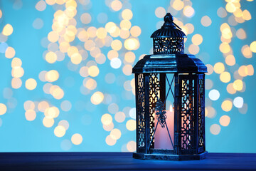 Traditional Arabic lantern on table against light blue background with blurred lights