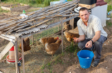 Positive man gathering chicken eggs outdoors. Farmer collecting eggs at henhouse. © JackF