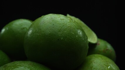 Slices of lime are meticulously arranged in a pile, set against a black background. Each lime slice is captured in stunning detail, its vibrant green hue and enticing texture. Close up. Comestible.