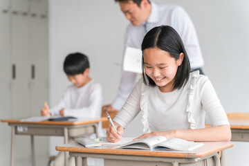 学校の教室で楽しく勉強する笑顔の高学年の小学生の男女（塾・夏期講習）と男性教師
