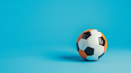 Fototapeta premium A classic black and white soccer ball with orange details lies on a blue studio background. The ball is slightly angled to the right of the frame.
