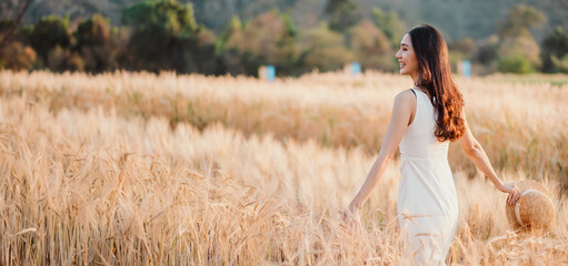 A woman is walking through a field of tall golden wheat. She is wearing a white dress and a straw hat. The scene is peaceful and serene, with the woman enjoying the beauty of the natural landscape © Satori Studio