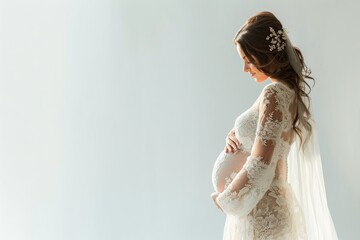 A pregnant woman stands in front of a white background wearing a white gown