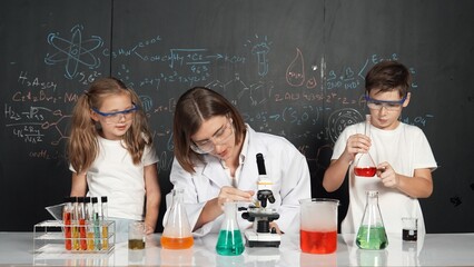 Caucasian boy mixing chemical liquid while teacher giving advice. Professional instructor wearing...