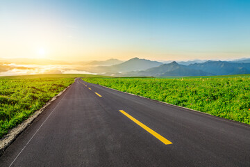 Asphalt highway road and green meadow with mountain nature landscape at sunrise