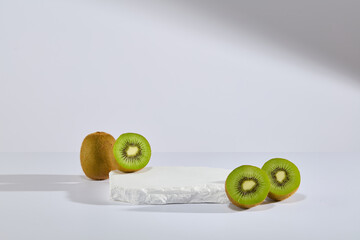 Against white background, a stone podium is decorated with some halves of kiwi fruit. Empty space...