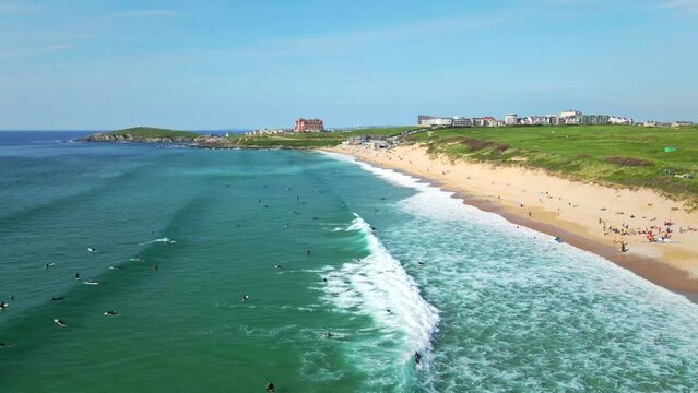 Fistral Beach Surfers Riding the Ocean Waves with Views of Headland Hotel and Golf Course, Newquay, UK. Aerial Panning Shot.