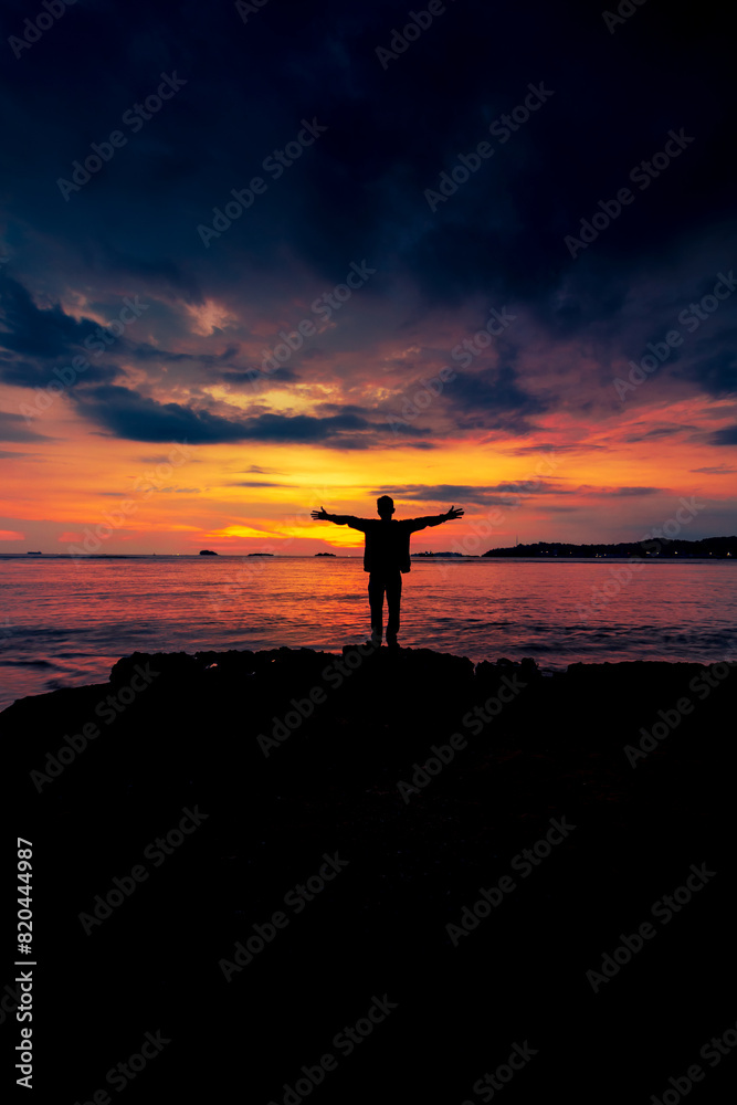 Sticker Silhouette of a man standing at shoreline looking at sunset 