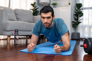 Athletic and sporty man doing plank on fitness mat during home body workout exercise session for...