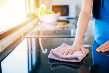 Young housewife smiles while disinfecting her kitchen table with a rag and detergent. Emphasizing...