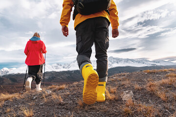 Two bright colorful tourists walks in rubber boots against mountains