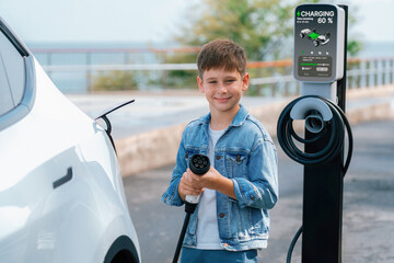 Little boy recharging eco-friendly electric car from EV charging station. EV car road trip travel...