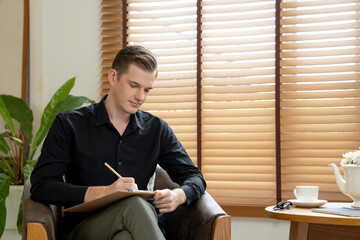 Portrait of happy and smiling male psychologist portrait sitting on arm chair in psychiatrist...