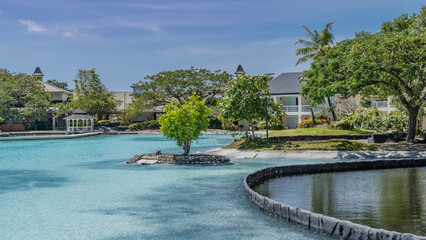 A relaxation area by the turquoise pool. A tree grows on an artificial island. A gazebo is visible...