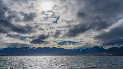 A picturesque snow-capped mountain range of the Andes against a cloudy sky. View from the Beagle Canal. Ripples and highlights on the water. Argentina. Tierra del Fuego Archipelago.
