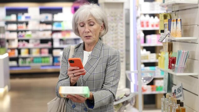 Interested old female client scanning QR of medical product held in hand in chemist's shop. High quality 4k footage