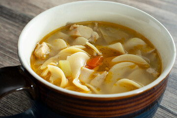 A closeup view of a mug of chicken noodle soup.
