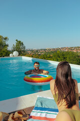 A man and a woman enjoying a pool overlooking a scenic town