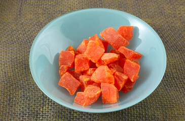 Orange dried papaya fruit chunks in blue snack bowl on burlap