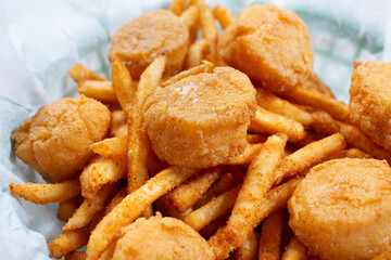 A closeup view of a basket of deep fried scallops and french fries.