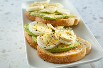 A closeup view of a plate of avocado toast, featuring slices of hard boiled eggs.