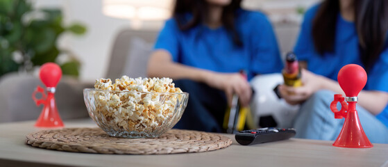 Lesbian couple cheering for Euro football at home with popcorn and air horn. Concept of LGBTQ pride, celebration, and sports excitement