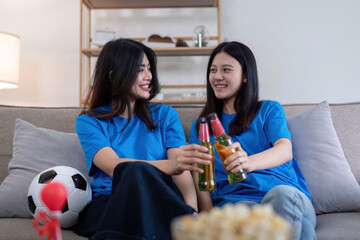 Lesbian couple cheering for Euro football with beers at home. Concept of LGBTQ+ pride, celebration, and sports enthusiasm