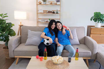 Lesbian couple cheering for Euro football match at home with drinks and popcorn. Concept of LGBTQ pride, sports enthusiasm, and celebration