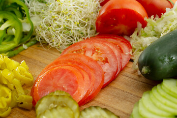A view of a stack of sliced tomatoes, among several other veggies on a wood board.