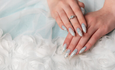 Elegant Hands Featuring Sparkling Ring and Blue Floral Manicure on Delicate White Fabric