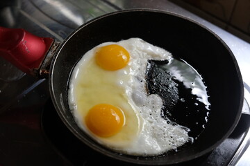 sunny side up eggs on a black frying pan on a gas stove. telur ceplok or mata sapi.