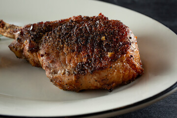 A closeup view of a bone-in Duroc pork chop on a plate.