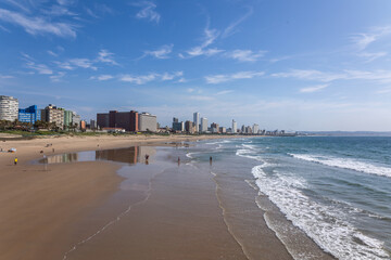 A perspective view of the beachfront with waves, exposed beach sand at low tide, city buildings and...