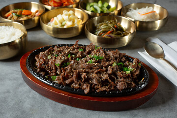 A view of a skillet plate of beef bulgogi, among several banchan bowls.