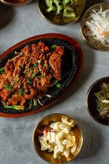 A top down view of spicy pork bulgogi among several banchan bowls.