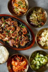 A top down view of a skillet plate of chicken bulgogi, among several banchan bowls.