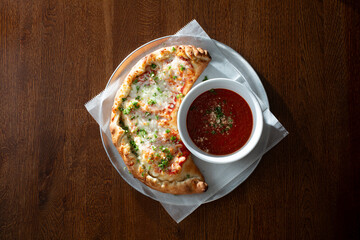 A top down view of a calzone entree, with a side of marinara dipping sauce.