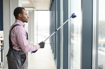 Happy Male Worker Cleaning Glass With Squeegee And Spray Bottle