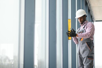 Low Angle View Of A Young African Repairman In Overalls Installing Window