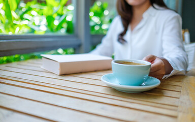 Closeup image of a woman drinking coffee with a book on table