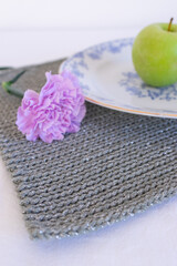 Green apple on blue and white plate. Table setting with gray wicker napkin and purple carnation, home decor close up